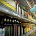 A person reaching for a bottle of olive oil on a grocery store shelf filled with various oils. - Olive Oil Times