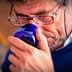 Man with glasses holding a blue glass cup to his nose, appearing to smell it. - Olive Oil Times