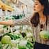 Woman selecting green onions while holding a cabbage in a grocery store produce section. - Olive Oil Times