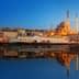 A ferry docked near a mosque in Istanbul during sunset with reflections on the water. - Olive Oil Times