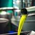 Fresh olive oil pouring from a metal spout into a container in a production facility. - Olive Oil Times