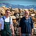 Two men posing in front of a stone wall with mountains in the background. - Olive Oil Times