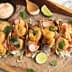 Five shrimp tacos topped with vegetables and sauce on a wooden serving board. - Olive Oil Times