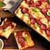 A rectangular pepperoni pizza topped with tomato sauce and fresh basil leaves, served in a baking tray. - Olive Oil Times