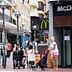A street scene featuring a McDonald's restaurant and pedestrians, including a woman with a stroller and a man on a mobility scooter. - Olive Oil Times