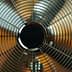 Close-up view of a metal oscillating fan with a wire grille and circular center. - Olive Oil Times