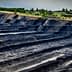 Aerial view of an open-pit mining site with layered black earth and machinery in the distance. - Olive Oil Times