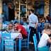 Outdoor dining area with tables and blue chairs at a restaurant, featuring patrons engaged in conversation. - Olive Oil Times
