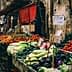 Market stall displaying various vegetables and fruits with price signs in a bustling market setting. - Olive Oil Times