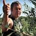 Man gesturing while standing among olive trees in an olive grove. - Olive Oil Times