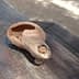 An ancient clay olive oil lamp with a spout and a round body resting on a wooden surface. - Olive Oil Times