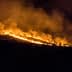 A hillside engulfed in flames during a wildfire, with smoke billowing into the night sky. - Olive Oil Times