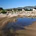 A metal bridge spans a riverbank with sandy terrain and a small pool of water in the foreground. - Olive Oil Times