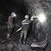 Two miners working in a dark underground mine with safety gear and tools. - Olive Oil Times