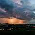 Lightning illuminating the sky over a landscape during dusk with dark clouds and distant lights. - Olive Oil Times