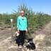 Woman wearing a green shirt and black pants standing with a black dog in an olive grove. - Olive Oil Times
