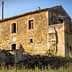 Abandoned stone house with a rustic exterior and overgrown vegetation in a rural area. - Olive Oil Times