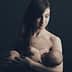 A mother gently cradling her baby in a dark background, both appearing calm and serene. - Olive Oil Times