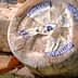 Round wheel of Castelmagno cheese with a blue and white label on a wooden surface. - Olive Oil Times