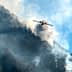 An aircraft releasing water to combat a wildfire in a mountainous region with smoke rising from the ground. - Olive Oil Times