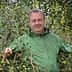 Man wearing a green jacket standing among olive trees with unripe olives. - Olive Oil Times