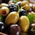A close-up of mixed green and black olives garnished with herbs in a wooden bowl. - Olive Oil Times