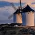Two traditional windmills with black blades and white stone structures situated on a hilltop. - Olive Oil Times
