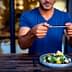 Individual holding a smartphone to take a photo of a salad dish on a wooden table. - Olive Oil Times