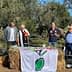 Four individuals speaking at an outdoor event with an olive-themed banner in front of them. - Olive Oil Times