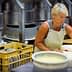 Woman in an apron handling cheese molds in a cheese production facility. - Olive Oil Times
