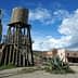 A wooden water tower stands beside a desert town with various buildings and a cactus. - Olive Oil Times
