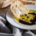 Slice of bread dipped in olive oil with balsamic vinegar on a white plate. - Olive Oil Times