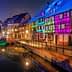 Row of half-timbered houses illuminated in various colors along a canal at night. - Olive Oil Times