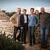 A group of six people standing together near a stone structure with a circular top. - Olive Oil Times