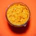 Glass jar filled with orange condiment on a bright orange background. - Olive Oil Times