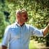Man in a light shirt examining an olive tree branch in a natural setting. - Olive Oil Times