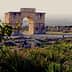 Stone archway structure at an archaeological site with surrounding ruins and greenery. - Olive Oil Times