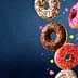 Four assorted donuts with chocolate, pink, and white icing, topped with sprinkles and colorful decorations. - Olive Oil Times