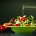 A bowl of mixed salad with cherry tomatoes and olive oil being poured over it. - Olive Oil Times
