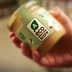 Hand holding a jar labeled with an eco score rating and a green logo. - Olive Oil Times