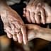 An elderly person's hands holding a younger person's hand, both adorned with rings. - Olive Oil Times