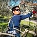 Individual wearing sunglasses and gloves pruning olive trees in a field. - Olive Oil Times