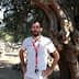 A man wearing a white shirt and lanyard standing beside a large olive tree. - Olive Oil Times