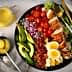 A colorful salad featuring grilled chicken, avocado, cherry tomatoes, and hard-boiled eggs on a black plate. - Olive Oil Times
