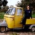 A person sitting on a yellow three-wheeled vehicle in an outdoor setting with trees. - Olive Oil Times