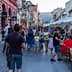 Crowd of people walking along a street with outdoor seating and shops in a town. - Olive Oil Times