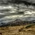 A mountain range under a dramatic cloudy sky with dark clouds and a barren landscape in the foreground. - Olive Oil Times