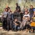 A group of twelve individuals posing together near an olive harvesting machine in an olive grove. - Olive Oil Times