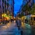 Narrow street in a European city illuminated by lights with outdoor dining areas and wet cobblestones. - Olive Oil Times
