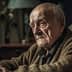 Elderly man with gray hair and a serious expression sitting on a couch in a dimly lit room. - Olive Oil Times